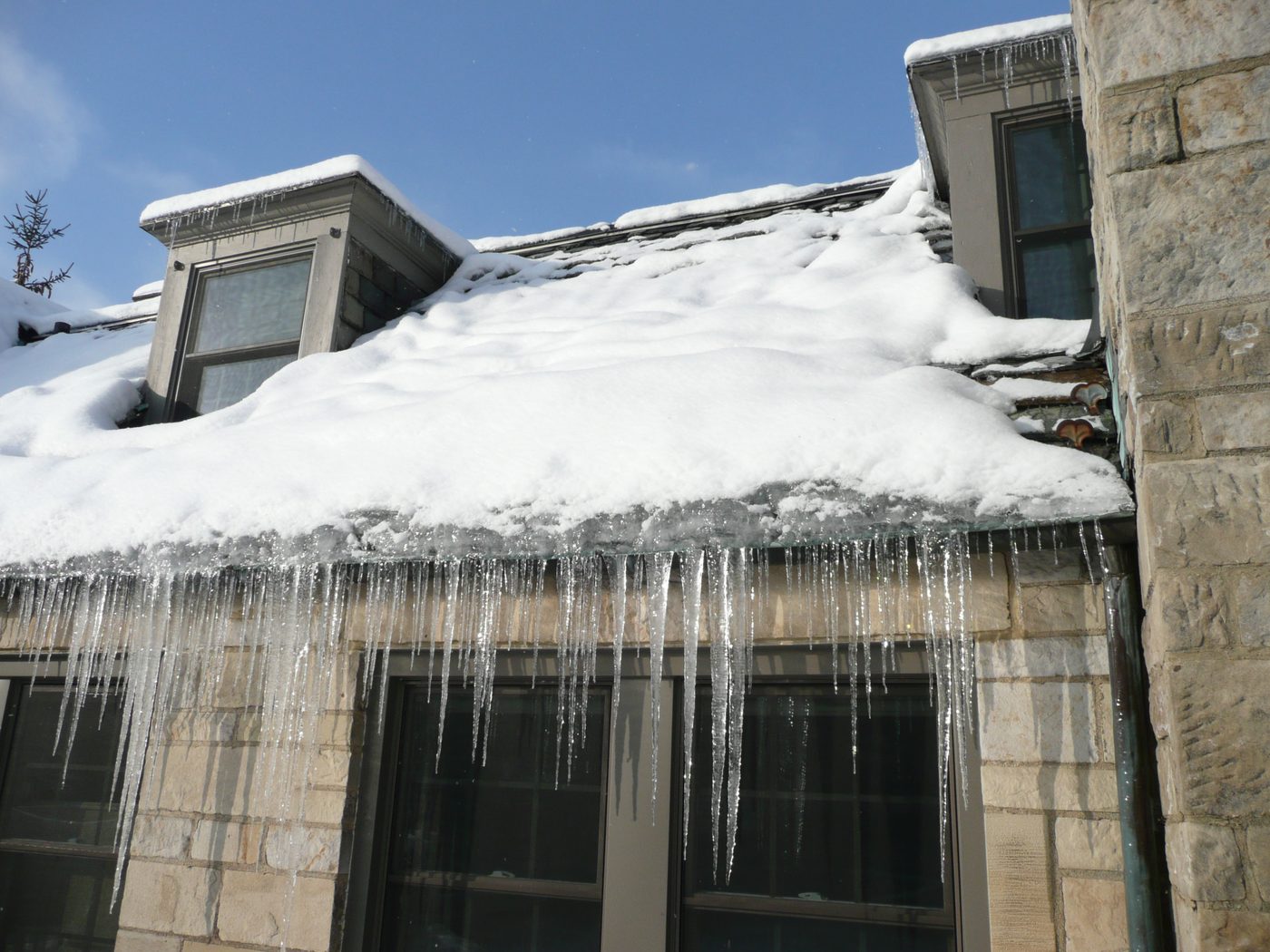 Thick band of ice at a snow-covered roof eave, with rows of icicles hanging from the edge